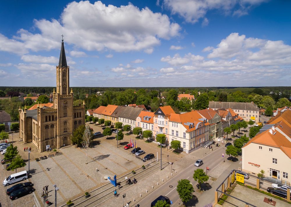 Das Foto zeigt den Marktplatz von Fürstenberg/Havel mit der Kirche bei schönem Wetter aus der Vogelperspektive.
